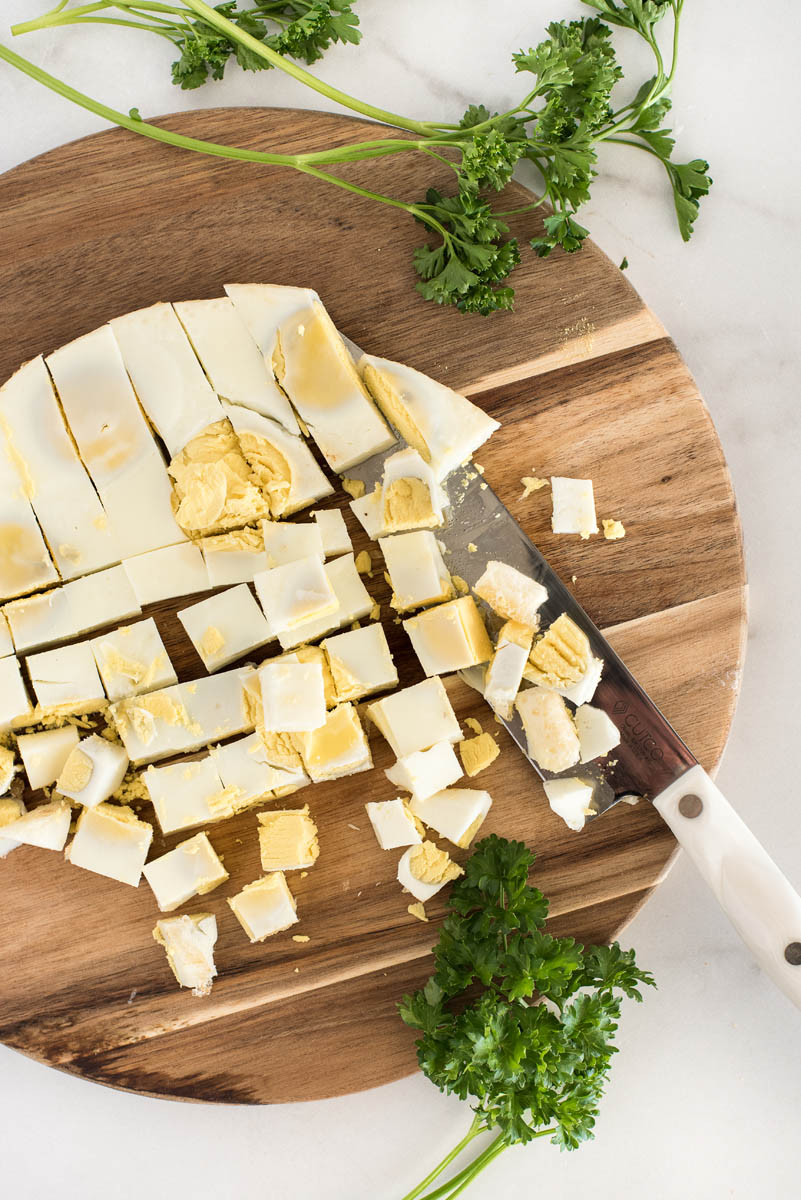 Dicing an Instant Pot egg loaf on a wooding cutting board with fresh parsley sprigs off to the side.