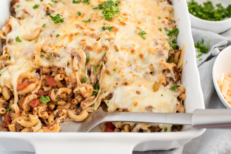 close up on melted cheese on top of ground beef and pasta casserole in a ceramic baking dish