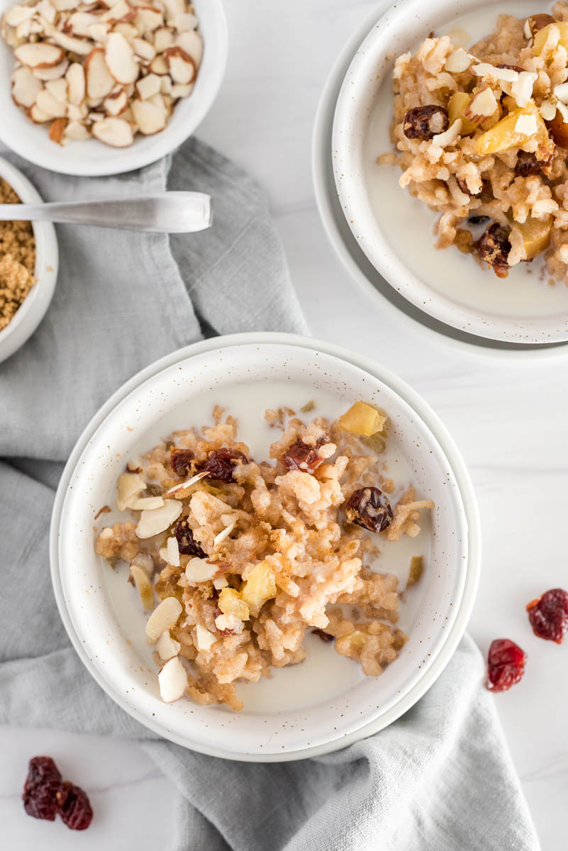 An overhead shot looking into a white bowl filled with apple risotto made in a pressure cooker, garnished with extra cinnamon and a splash of milk