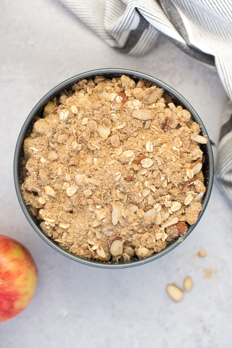 an overhead shot of the Instant Pot apple crisp topped and ready to go in the INstant Pot with a red apple and a white striped napkin in the background