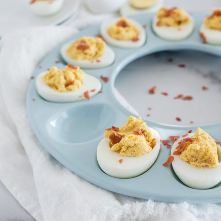 45 degree overhead of a blue circular egg tray filled with Instant Pot BBQ deviled Eggs with crumbled bacon with one egg removed.