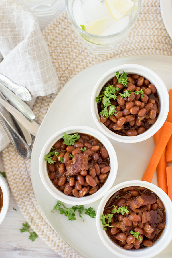 Three white ramekins filled with Instant Pot baked beans served with celery and carrot sticks on the side