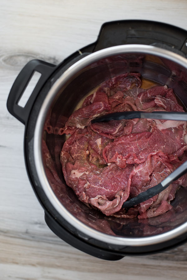 Overhead of an instant pot with raw thinly sliced beef beofre pressure cooking to make sandwiches