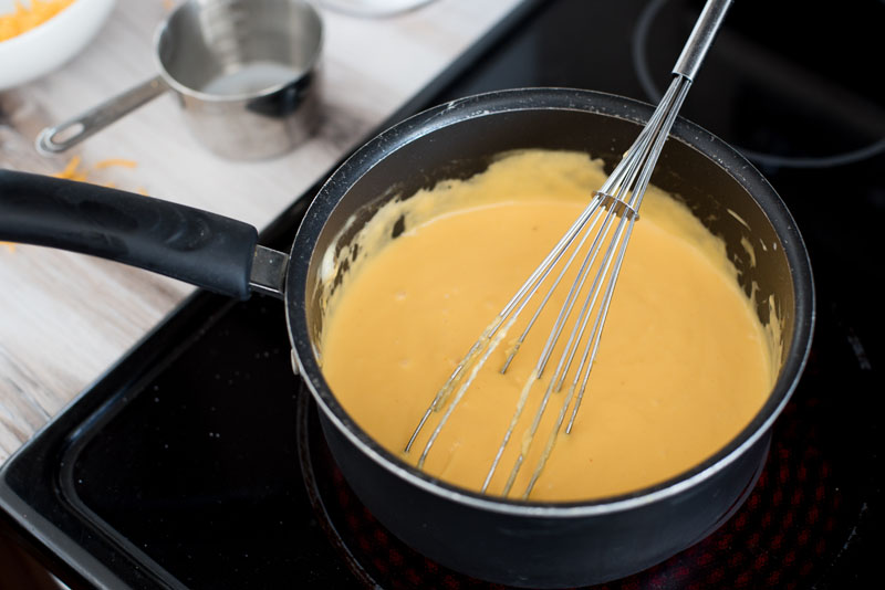 melted cheddar cheese sauce in a saucepan on the stove being whisked