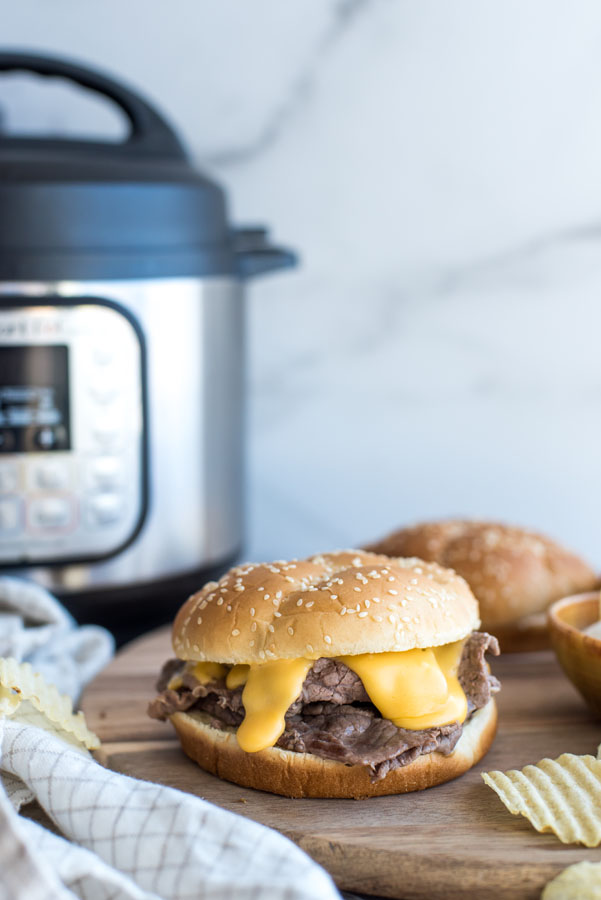 sliced beef and melted cheddar cheese sandwiches on a cutting board in front of an Instant Pot pressure cooker