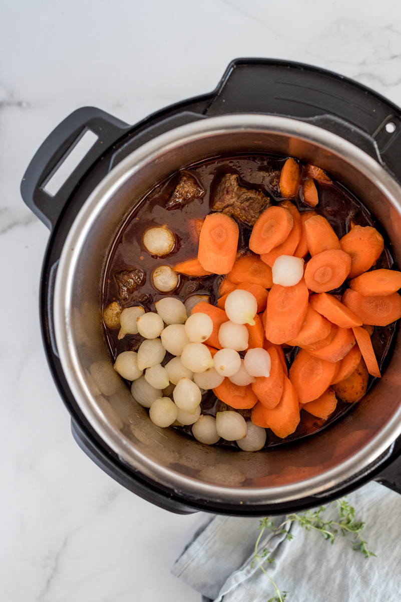 Adding the carrots and pearl onions to the beef bourguignon cooking in an Instant Pot.
