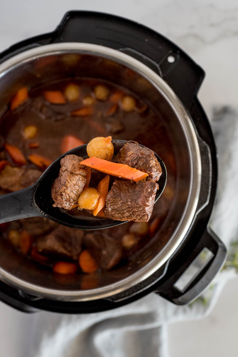 Beef bourguignon cooked in an Instant Pot with the beef, carrots and pearl onions on a spoon.