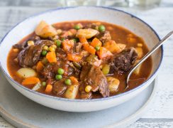 A bowl of Pressure Cooker Beef Stew with chunky potatoes, carrots, and peas in a bowl with a spoon.