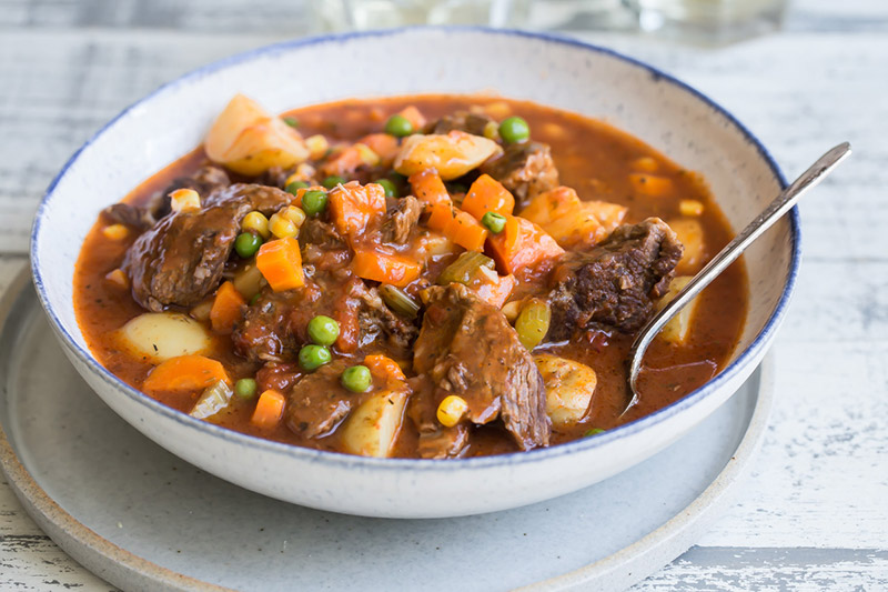 A bowl of Pressure Cooker Beef Stew with chunky potatoes, carrots, and peas in a bowl with a spoon.