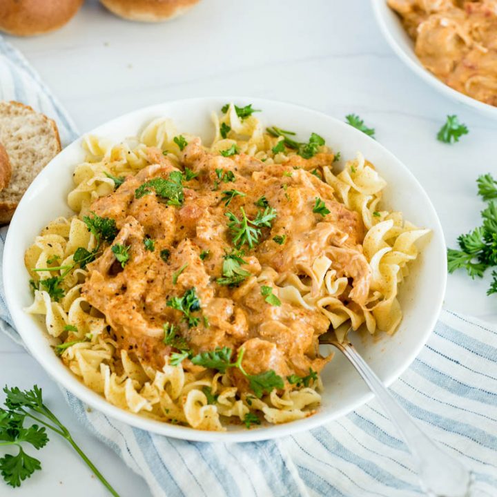 A bowl of Instant Pot paprika chicken made from frozen chicken, and ready to eat served on top of egg noodles with fresh parsley on top.