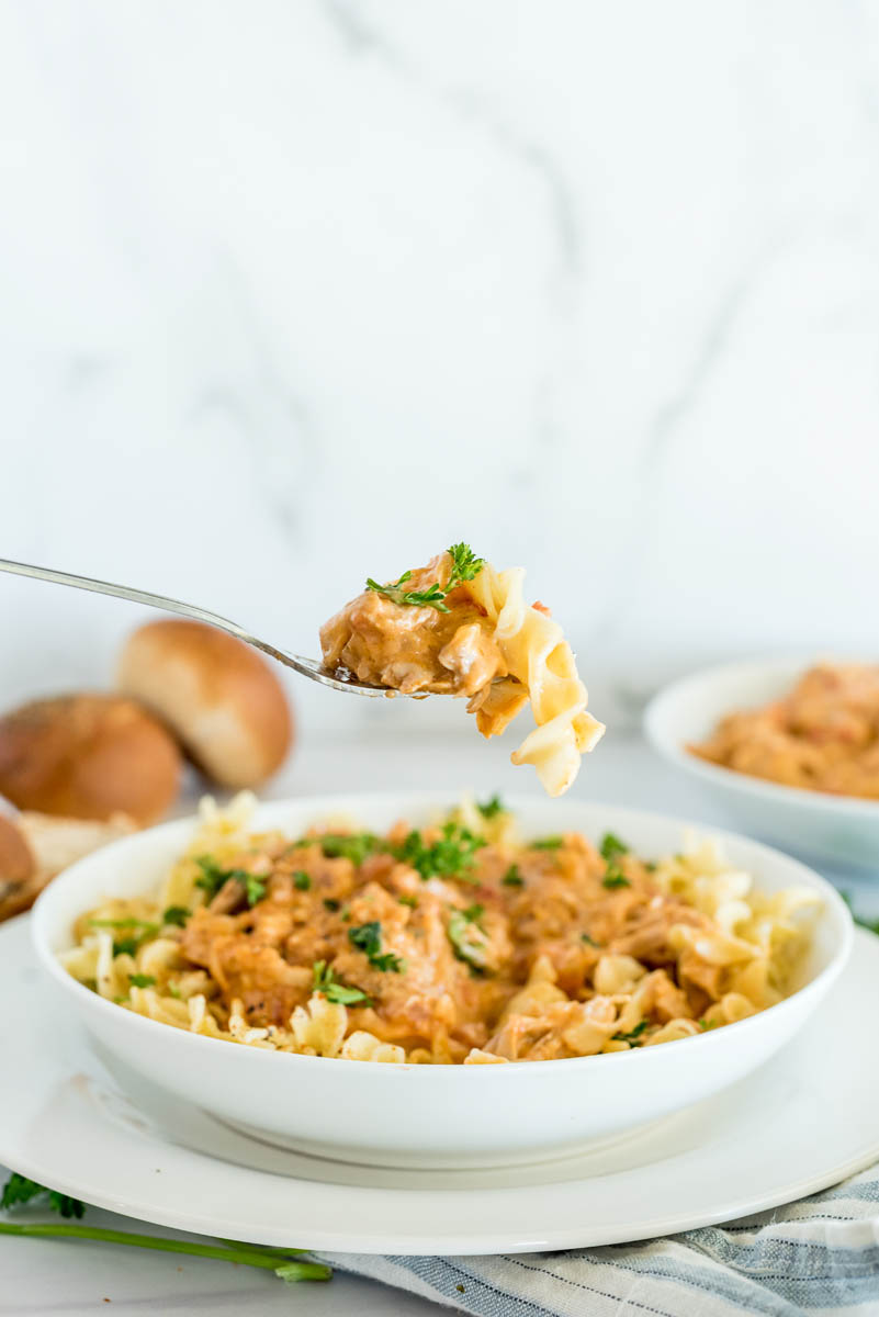 Instant Pot paprika chicken served in a bowl with egg noodles with a bite on a fork, ready to eat.