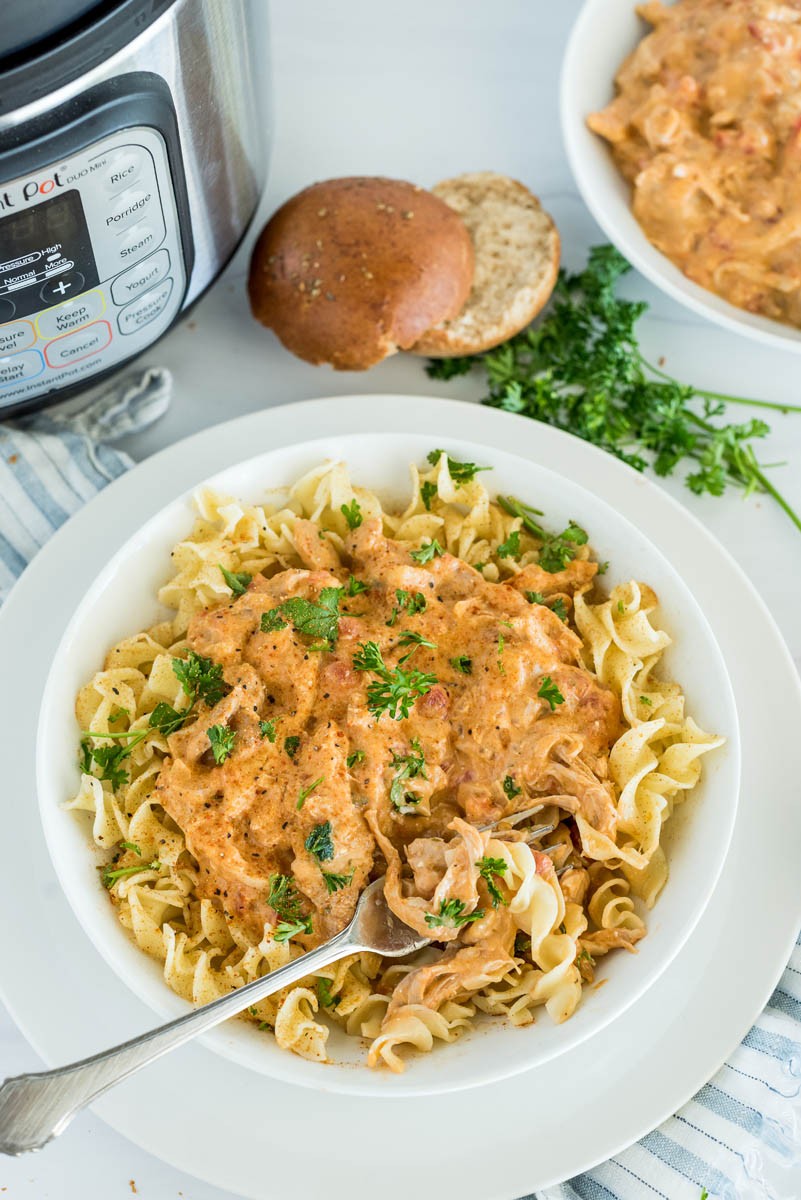 Overhead shot of pressure cooker paprika chicken served over egg noodles and served with fresh parsley, placed in front of an Instant Pot.