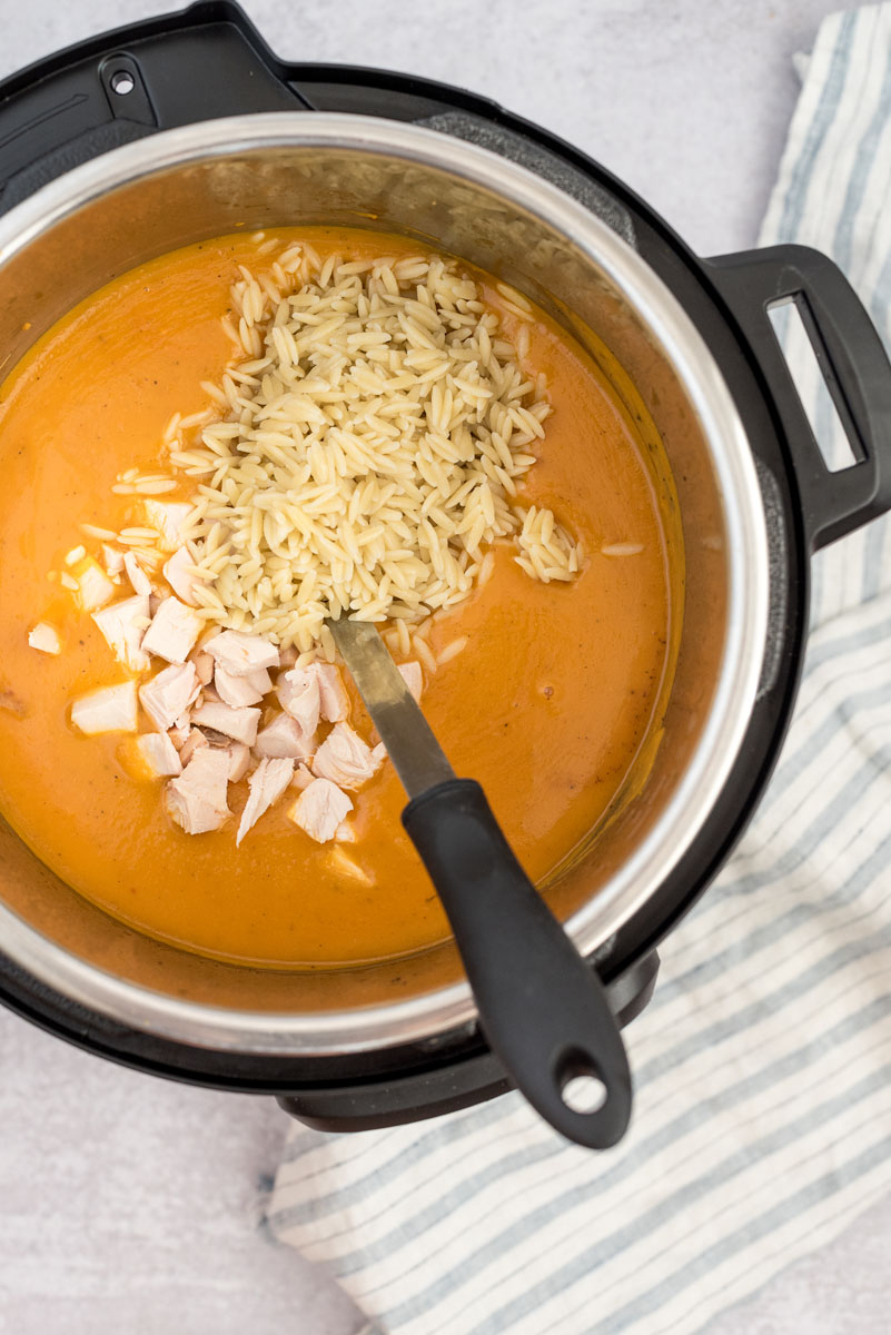 an overhead shot of the orzo pasta and the diced chicken being added to the soup