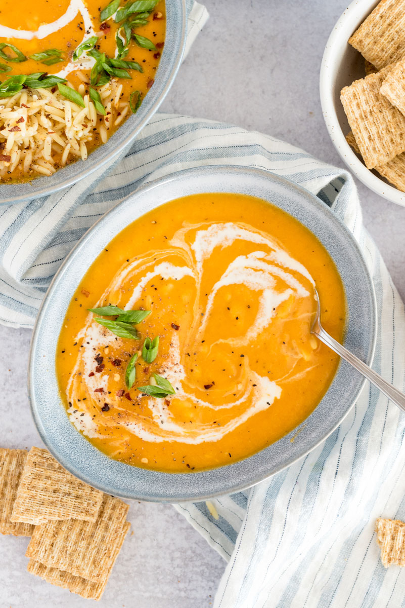 close-up of the butternut squash soup in an egg-shaped bowl, with a swirl of cream and the chicken and pasta mixed in with a larger bowl of soup in the background