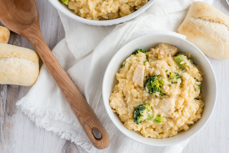 Overhead shot of cheesy chicken and broccoli casserole made in an instant pot, placed in a white bowl for serving, next to a wooden spoon.