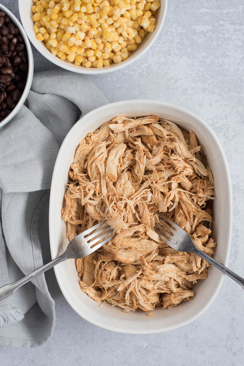 Shredded chicken for Instant Pot Chicken Enchilada Soup next to a bowl of corn and a bowl of beans.