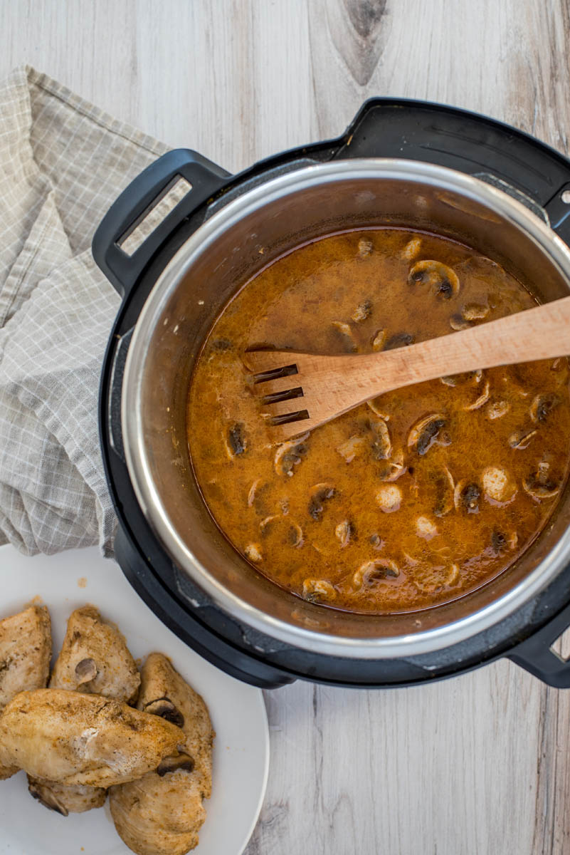 stirrng creamy mushroom sauce in an instant pot with a wooden spoon