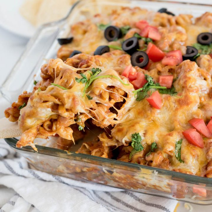 Instant Pot chicken enchilada pasta being scooped from a serving dish using a wooden spoon.