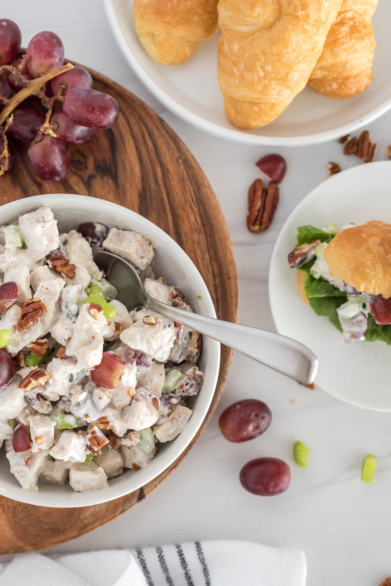 overhead of a white bowl with chicken salad and grapes, pecans and croissant rolls