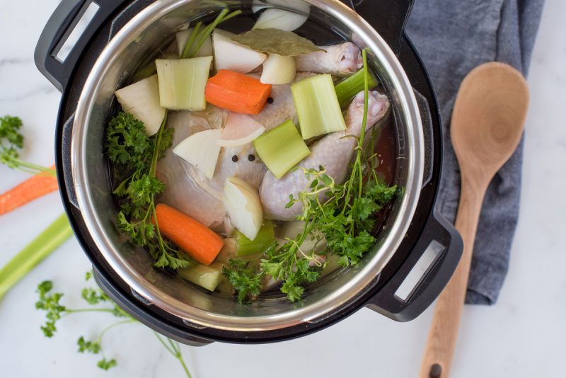 overhead of an instant pot cooking chicken stock with carrots, celery, onions and fresh herbs