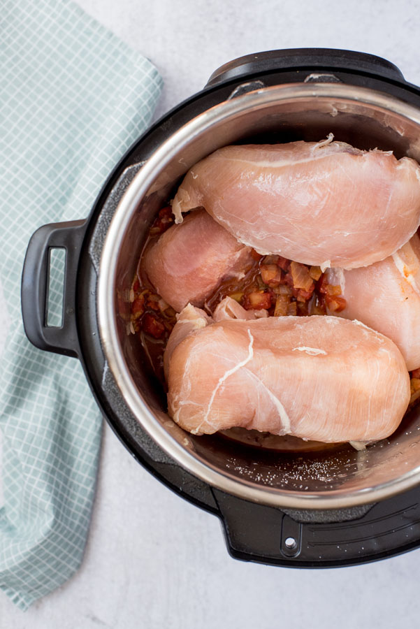 An Instant Pot cooking pot filled with frozen chicken breasts, diced tomatoes, ready to be made into easy Instant Pot shredded chicken tacos