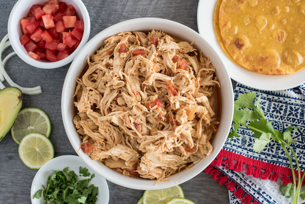 Pressure Cooker chicken taco filling, with diced tomatoes, cilantro, avocado, limes, and corn tortillas