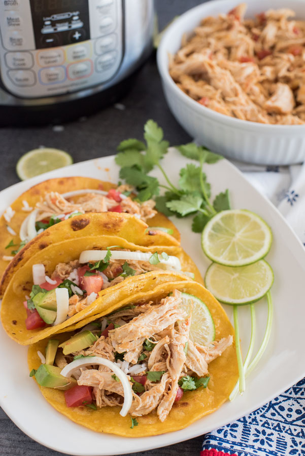 Easy Instant Pot Chicken Tacos on corn tortillas with a bowl of additional shredded chicken taco meat and an Instant Pot in the background