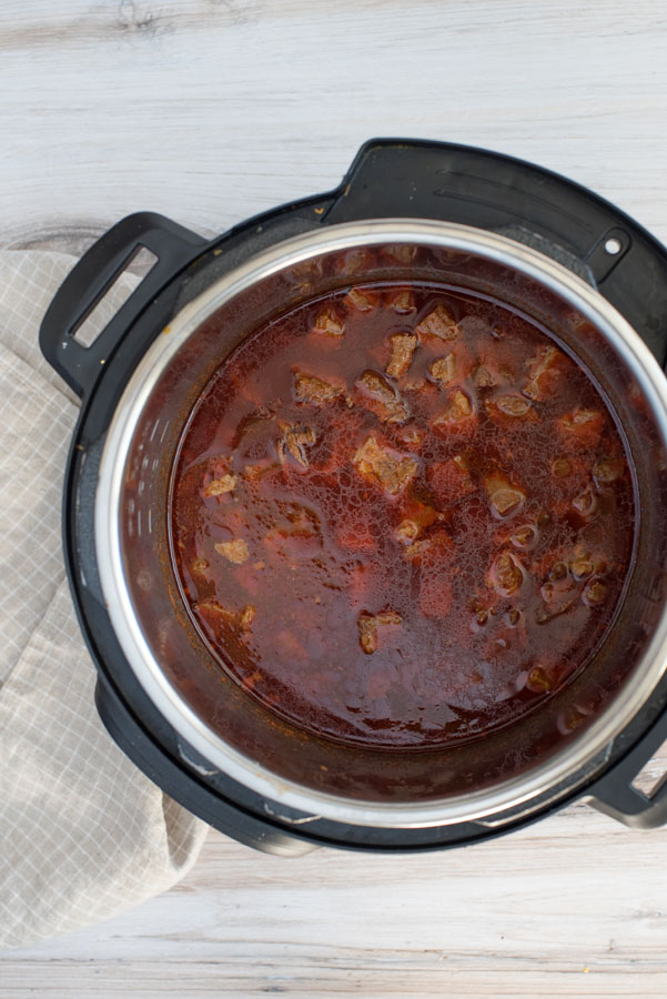 Overhead of an Instant Pot with red Colorado Chile made from cubed beef rump roast, enchilada sauce and beef bouillion.