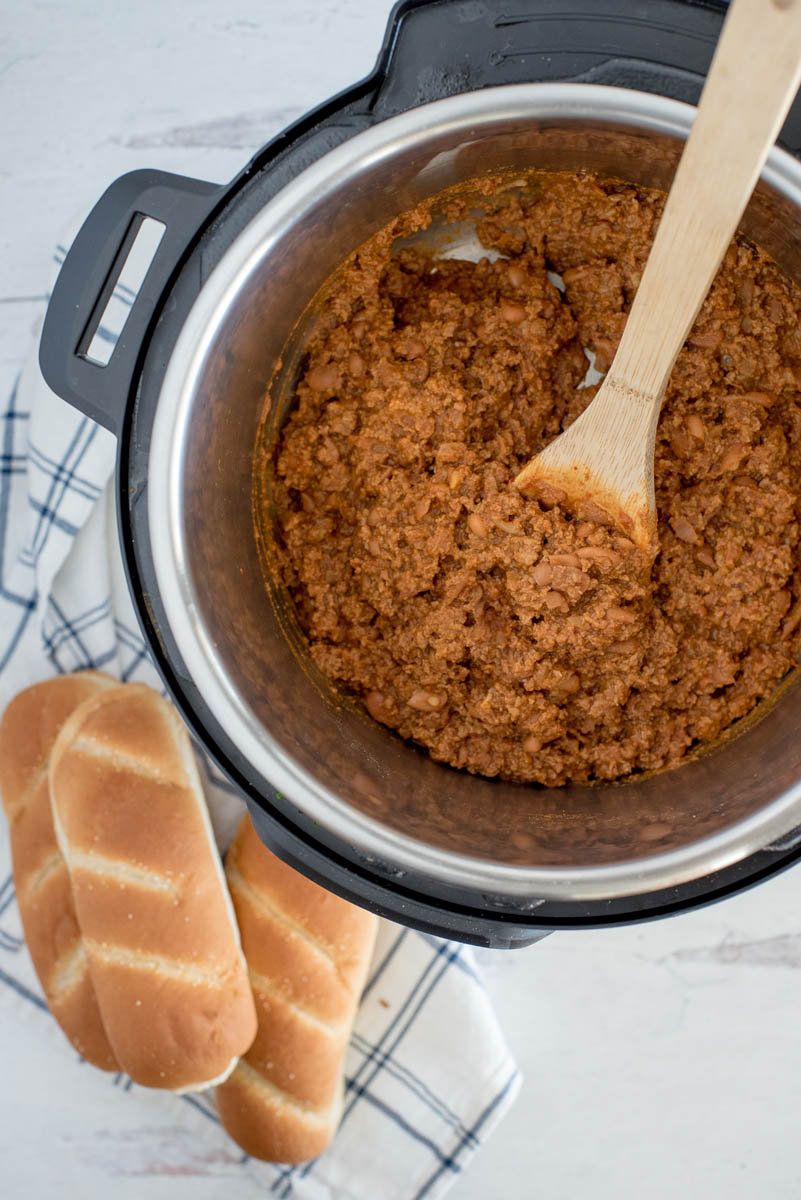 wooden spoon stirring bean and meat chili in a pressure cooker