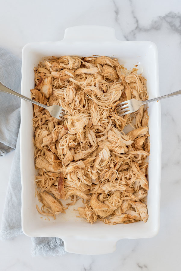 Overhead shot of shredded chicken on a white platter using forks.