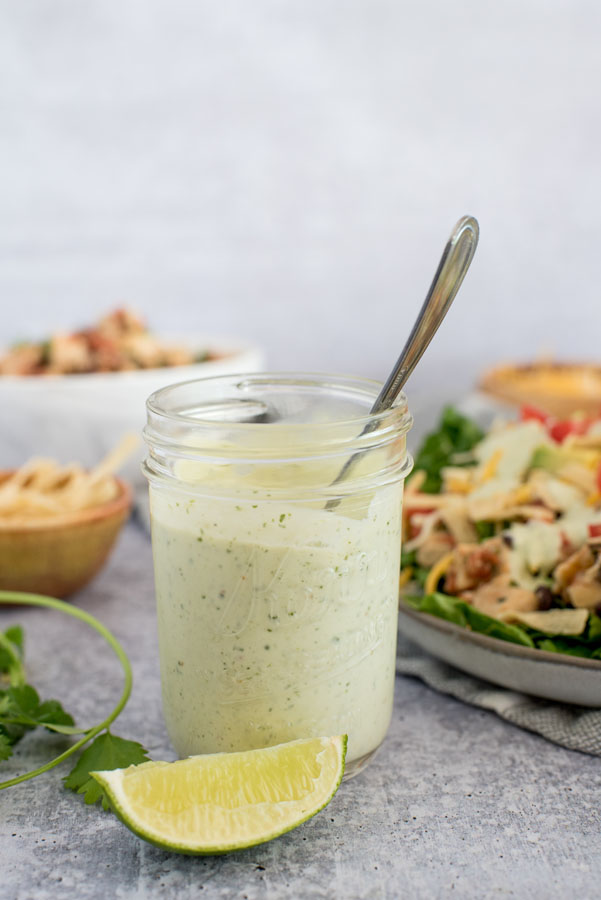 glass jar of green cilantro lime dressing with a lime wedge