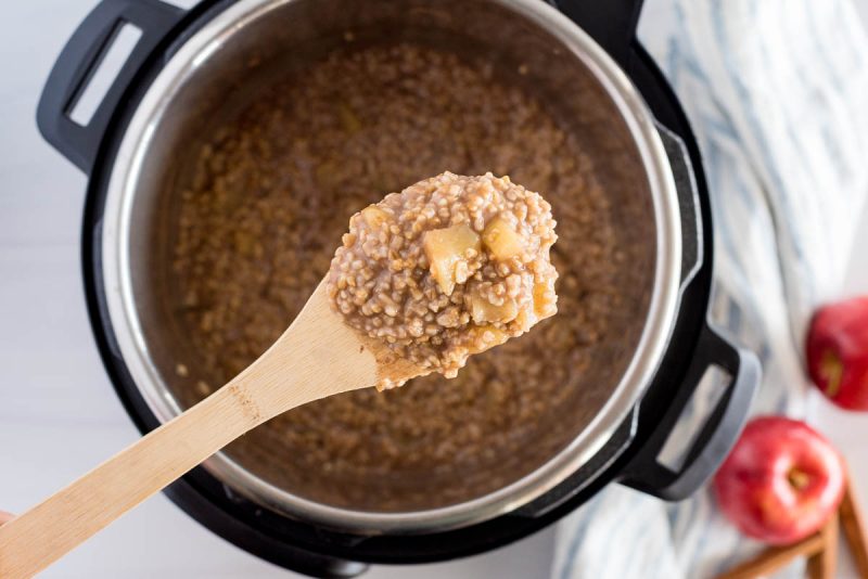 overhead of instant pot steel cut oats with apples on a wooden spoon with a pressure cooker in the background