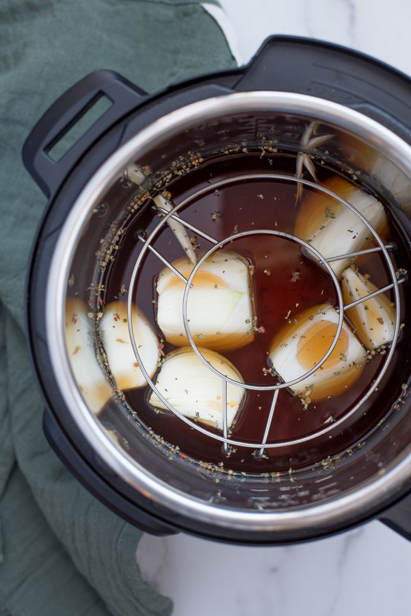 Overhead of an Instant Pot filled with seasoning, beef broth, and white onions with a rack set inside for cooking pressure cooker corned beef and cabbage.