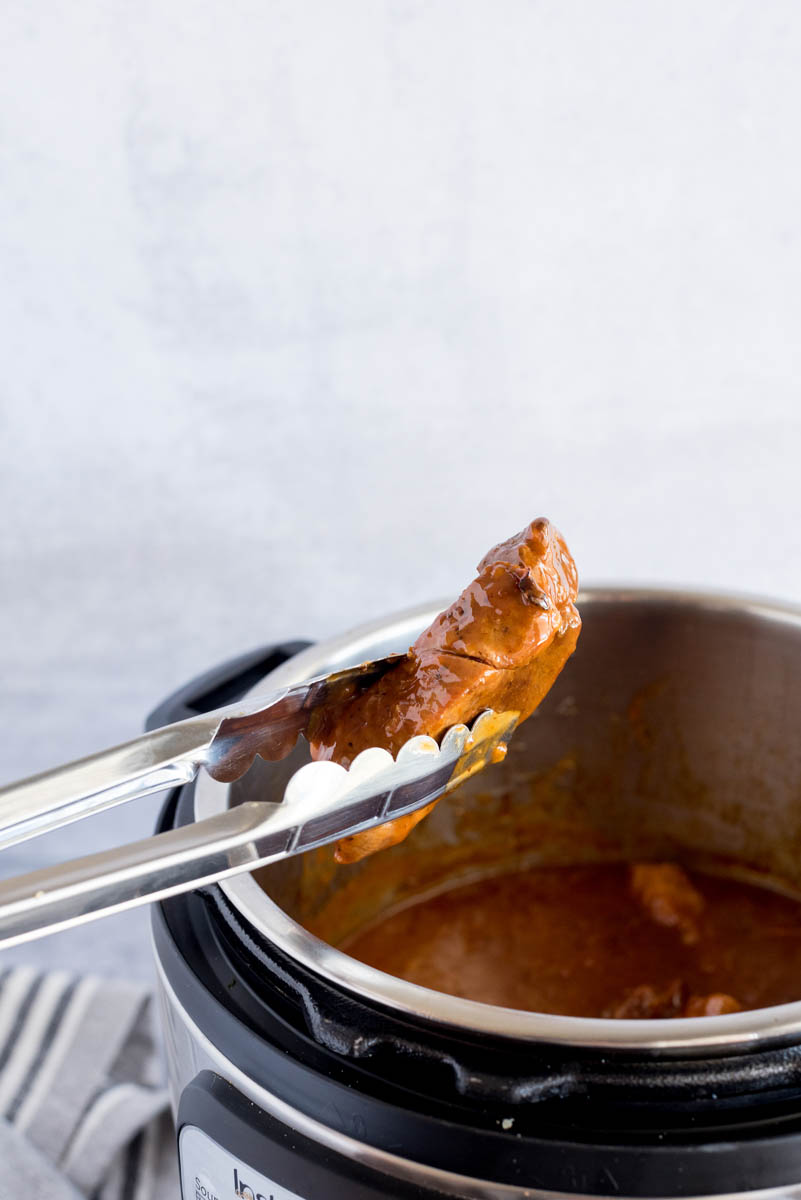 tongs removing pork ribs from an instant pot