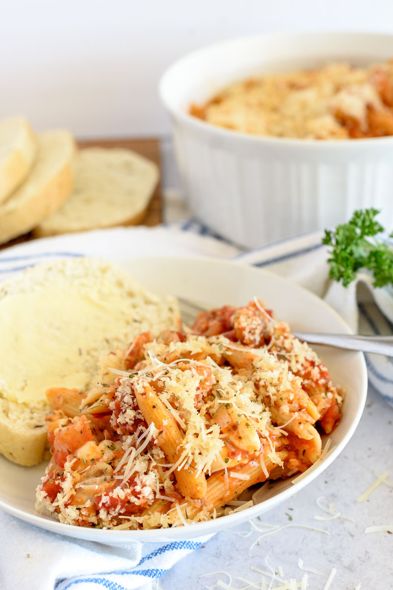 Pressure Cooker eggplant parmigiana plated next to garlic bread and placed front of sliced bread and the serving dish.