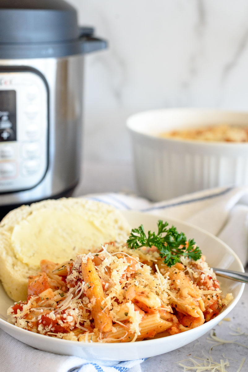 Eggplant parmigiana plated next to garlic bread and garnished with fresh parsley, and placed in front of an Instant Pot.