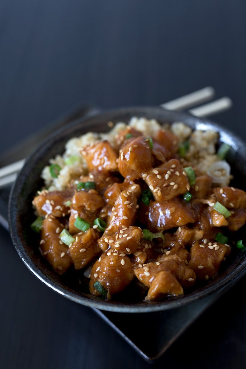 A close-up of Honey Sesame Chicken in a dark black bowl against a dark black background