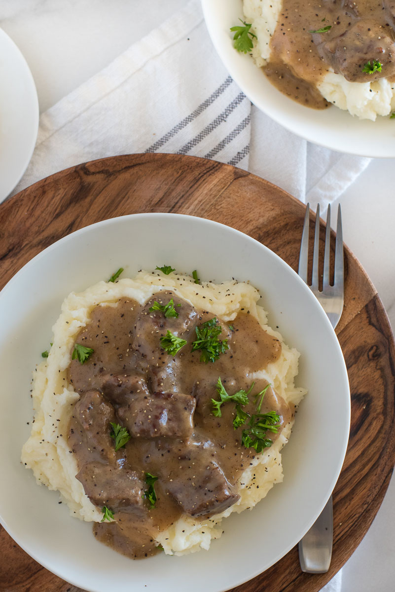 swedish kalops in a white bowl over mashed potatoes with fresh parsley