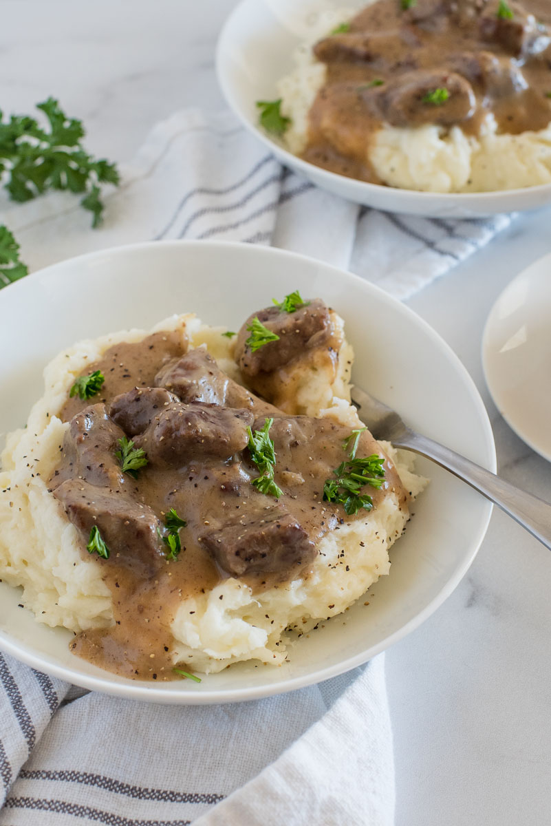 serving of swedish beef stew over mashed potatoes in a white bowl