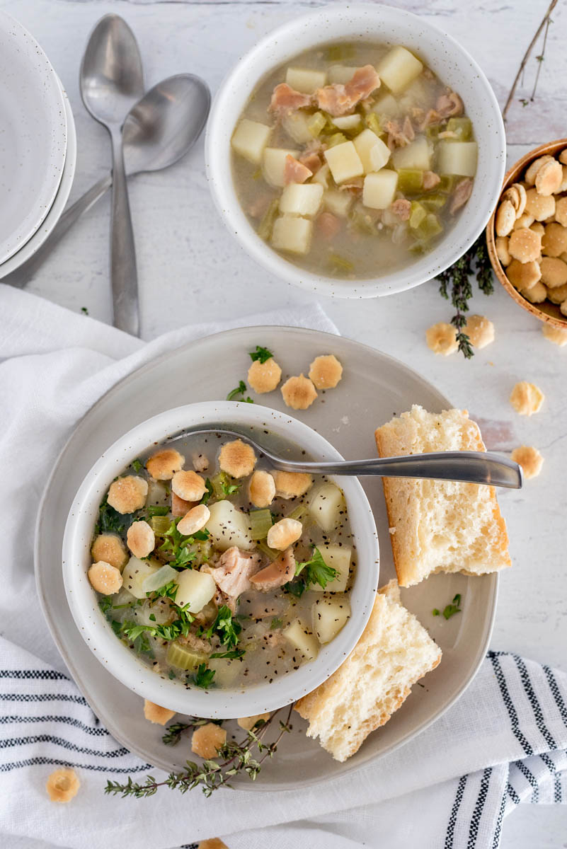 Overhead shot of Instant Pot light clam chowder garnished with oyster crackers and parsley, served in a white bowl with a roll.