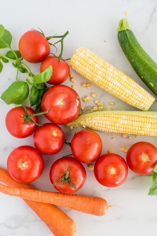 Overhead shot of garden fresh vegetables, including tomatoes, carrots, corn, and zucchini for making minestrone soup.