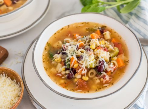 45 degree angle picture of pressure cooker minestrone soup topped with parmesan, in a white bowl.