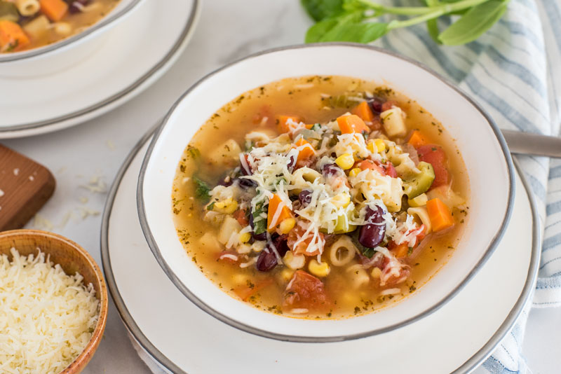 45 degree angle picture of pressure cooker minestrone soup topped with parmesan, in a white bowl.