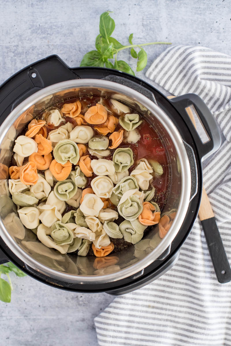 Frozen tortellini added to an Instant Pot with a homade tomato and basil sauce ready to cook.