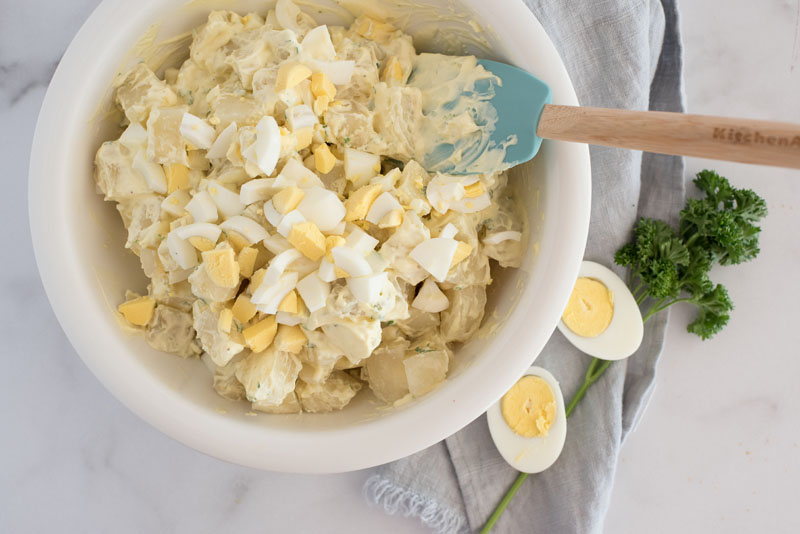 overhead of a white mixing bowl where instant pot poato salad is being mixed with homemade mayonnaise dressing