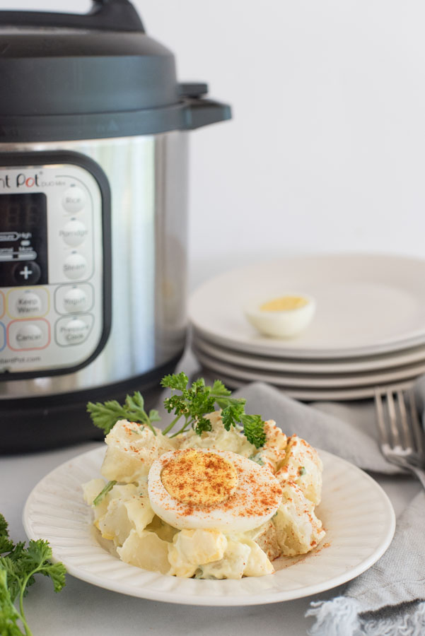 side view of instant pot potato salad with hard boiled eggs and fresh parsley infront of an electric pressure cooker