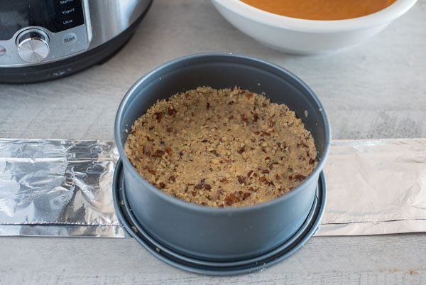 Pecan Sandy cookie crust in the bottom of a spring from pan, in front of an Insta Pot