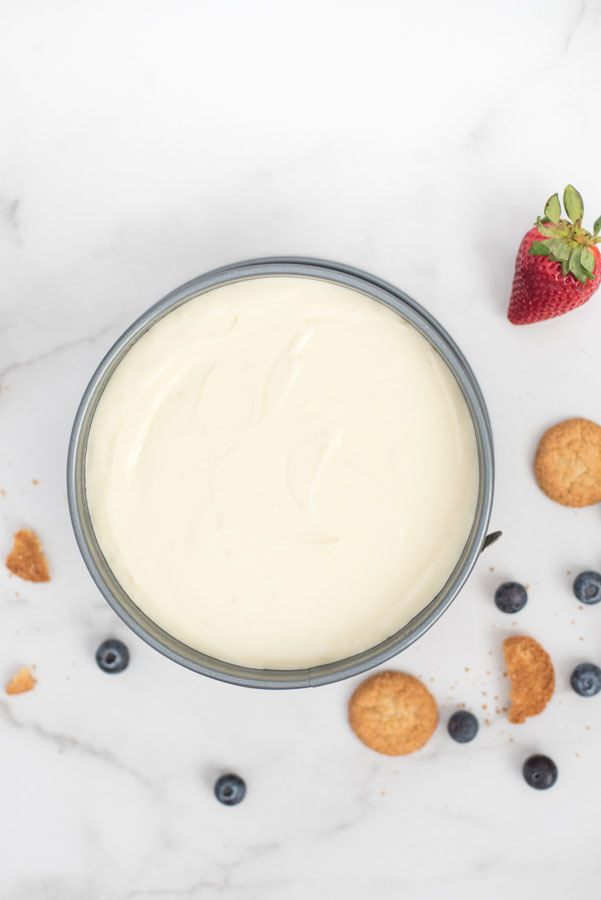 Overhead shot of a baked cheesecake in spring form pan with fresh berries and cookies scattered around it.