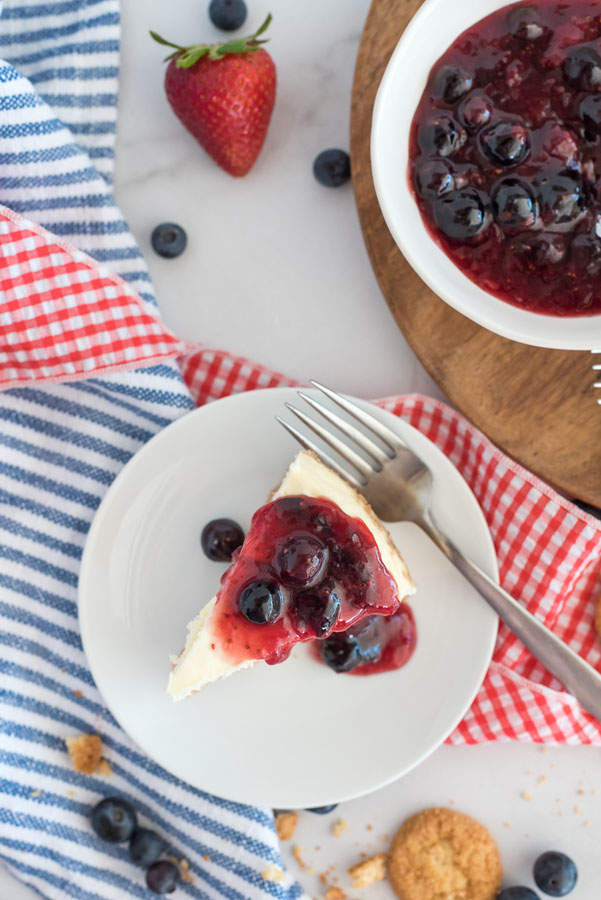 Overhead shot of plated slice of cheesecake topped with fresh berry compote over red, white and blue napkins.