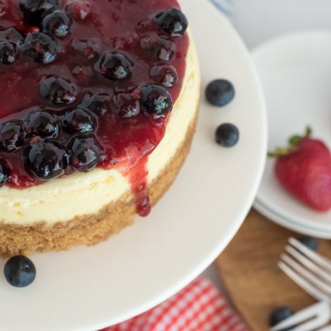 Close up overhead shot of Instant Pot cheesecake topped with triple berry compote on a white cake stand